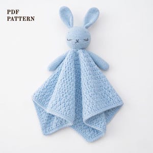 Può includere: Una coperta di sicurezza a forma di coniglietto all'uncinetto blu chiaro. Il coniglietto ha lunghe orecchie, occhi chiusi e braccia piccole. La coperta è di forma quadrata con un motivo strutturato. Il testo "PDF PATTERN" è nell'angolo in alto a sinistra.