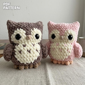 May include: Two crocheted owl figurines. One is brown and cream, the other is pink and cream. Both have large black eyes and small beaks. The owls are sitting on a neutral-coloured surface. The words "PDF PATTERN" are in the upper left corner.