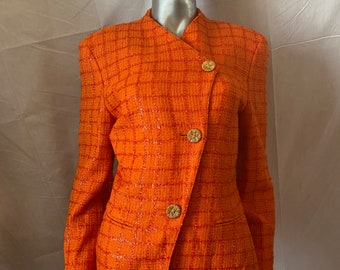 May include: A bright orange blazer with a checkered pattern and gold buttons. The blazer has a slightly asymmetrical design and a long, flowing silhouette.