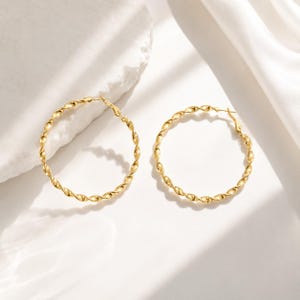 Pair of polished gold-tone hoop earrings with a twisted rope-like texture, round silhouette, and post-back closures.
