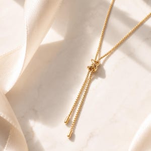 Dainty 18K gold PVD bolo necklace with an adjustable sliding chain, polished minimalist finish, and delicate drop ends.