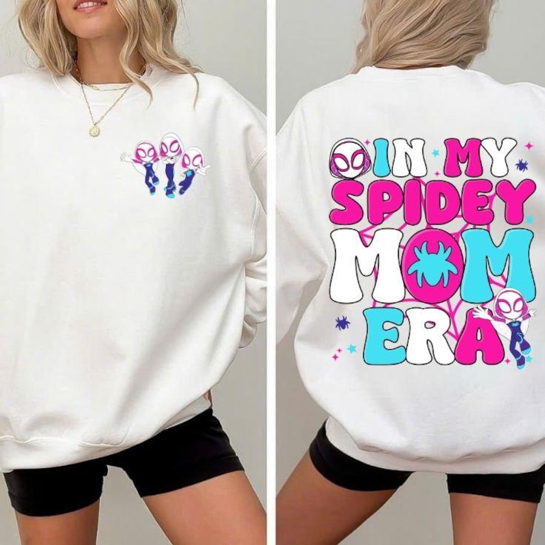 Peut inclure: Sweat-shirt blanc avec un motif de Spider-Gwen. L'avant pr&eacute;sente un graphisme des personnages de Spider-Gwen, tandis que l'arri&egrave;re affiche le texte "IN MY SPIDEY MOM ERA" en rose, bleu et blanc. Le design est lumineux et color&eacute;.