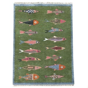 May include: A rectangular green rug with a repeating pattern of colorful fish. The fish are in various colors, including red, orange, blue, and purple. The rug has a blue border and a fringed edge.