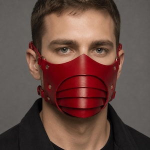 May include: A deep red leather face mask featuring a layered, gill-like structure over the mouth area. The mask is secured with thin leather straps, metal rivets, and circular rings on the sides, covering the nose and mouth with a pointed bridge.