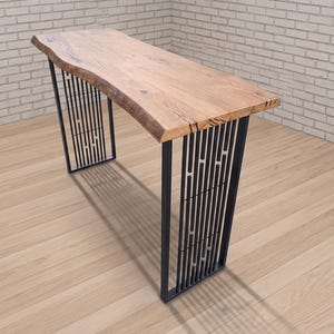May include: A wooden desk with a live edge top and black metal legs. The desk's tabletop is a light brown color with a natural edge. The legs are made of black metal bars arranged in a vertical pattern.