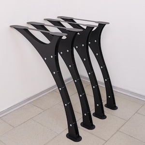May include: A set of four black metal table legs with a curved, tapered design. Each leg features a flat mounting plate at the top, a wide base at the bottom, and is constructed with multiple visible silver-colored rivets along the side frame.