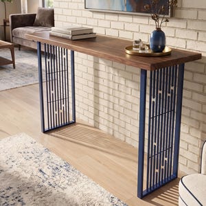 Op de afbeelding: Een rechthoekige sidetable met een donkerbruin houten blad en twee marineblauwe metalen poten met een verticaal lattenontwerp. Op het tafelblad staan twee gestapelde boeken, een gouden rond dienblad en een blauwe vaas met droge takken.