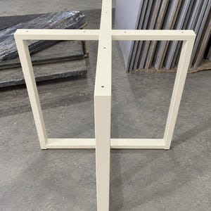 Può includere: Una base per tavolo in metallo bianco dal design a croce, dotata di quattro gambe verticali collegate da una struttura di supporto centrale. Il telaio è realizzato in tubolari quadrati e presenta fori preforati per il fissaggio del piano.