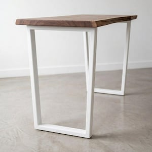 May include: A rectangular table featuring a natural dark brown wood slab top with a live edge finish. The table is supported by two white metal U-shaped legs that provide a stable base. The wood grain is visible across the surface of the top.