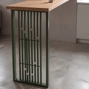 May include: A table with a light-toned wooden top and a rectangular base made of olive green metal. The base features a series of vertical metal bars of varying lengths arranged in a repeating pattern within a solid rectangular frame.