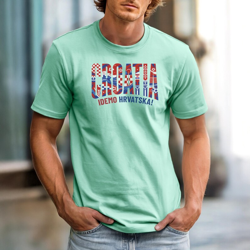May include: A light green t-shirt with the word "CROATIA" in a colorful, patterned design. Below the word is the phrase "IDEMO HRVATSKA!" in white. The shirt is short-sleeved.