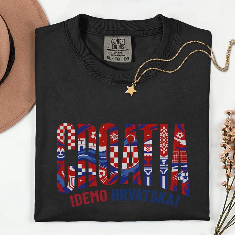 May include: Black Comfort Colors t-shirt with the word "CROATIA" in red, white, and blue, featuring various Croatian-themed designs. The text "IDEMO HRVATSKA!" is below. A gold star pendant necklace and a brown hat are also visible.