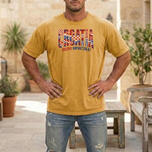 May include: Mustard yellow t-shirt with the word "CROATIA" in a multi-colored design, and the text "IDEMO HRVATSKA!". The shirt is a short-sleeved crew neck style.