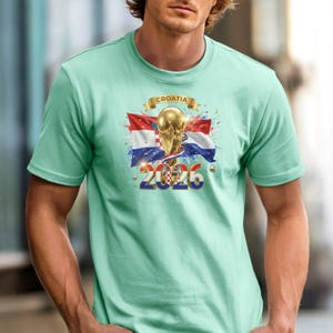 May include: A light green t-shirt featuring a graphic design with the Croatian flag, a golden trophy, and the year "2026". The word "CROATIA" is printed above the trophy on a gold banner. The design includes red, white, and blue colors.