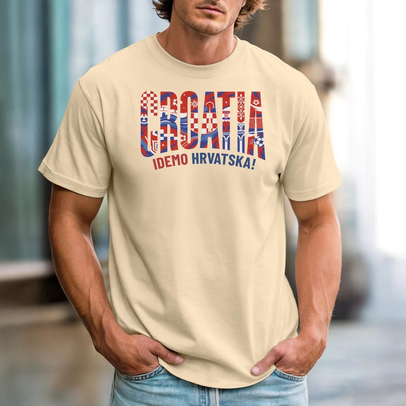 May include: A light beige t-shirt with the word "CROATIA" in red, white, and blue block letters. Below the word "CROATIA" is the phrase "IDEMO HRVATSKA!" in white letters. The t-shirt is short-sleeved.