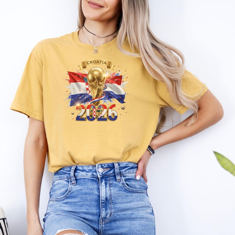 May include: Mustard yellow t-shirt featuring a graphic of the Croatian flag, a gold trophy, and the text "2026". The word "Croatia" is printed above the trophy. The shirt has short sleeves and a crew neck.