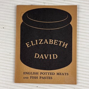Peut inclure: Une couverture de livre vintage marron et noire. Elle présente une illustration de pot noir avec les mots "ELIZABETH DAVID" en police serif. Le texte en dessous indique "ENGLISH POTTED MEATS AND FISH PASTES".