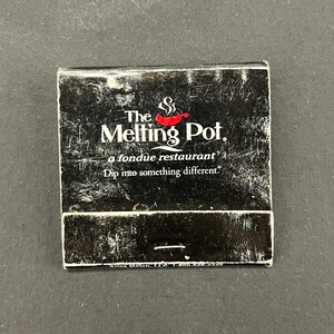 May include: A black matchbook from "The Melting Pot" fondue restaurant. The logo features a red chili pepper and the text "The Melting Pot" in white. The tagline "Dip into something different" is also visible.