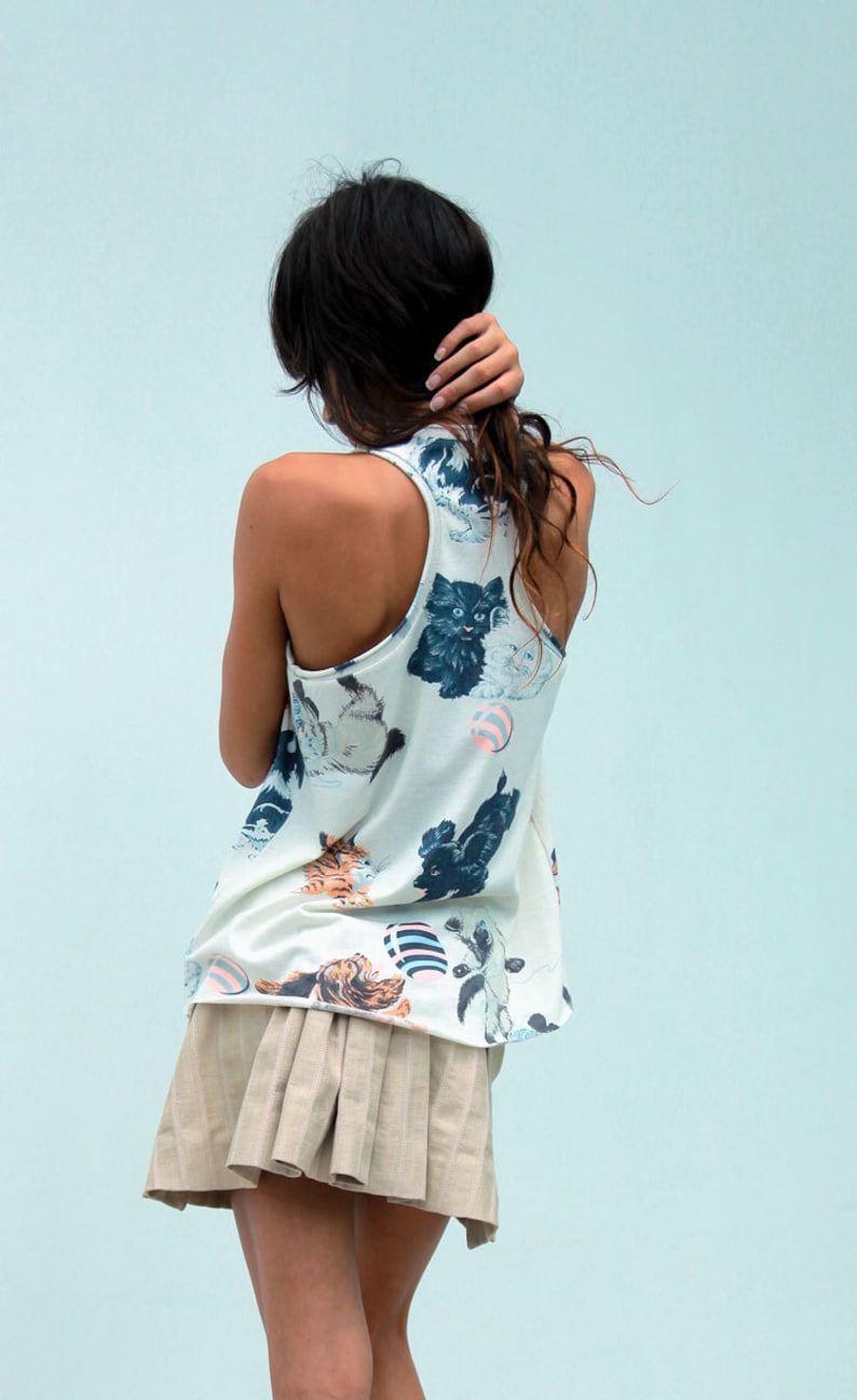 May include: A woman wearing a white tank top with a cat print and a beige pleated skirt.