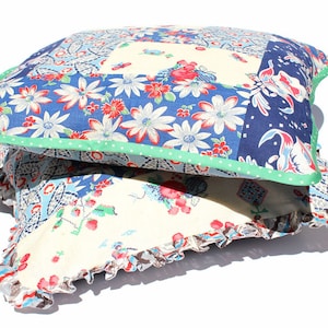 May include: Two decorative throw pillows with a patchwork design. The top pillow has a blue, green, and white floral pattern with a green trim. The bottom pillow has a white background with a blue and red floral pattern and a brown ruffle trim.