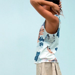 May include: A woman wearing a white tank top with a colorful cat print and a beige pleated skirt.