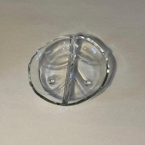 Puede incluir: Un plato de servir de vidrio transparente dividido con forma de hoja. El plato está dividido en tres secciones, con un diseño redondeado en relieve en cada sección. Los bordes del plato son ligeramente festoneados.