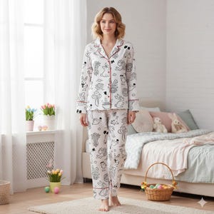 以下が含まれることがあります： イースターをテーマにした黒いイラストが施された白いパジャマセット。長袖トップスとパンツには、ウサギ、卵、その他の休日のモチーフが繰り返されるパターンがあります。赤いトリムが襟、袖口、ポケットを強調しています。