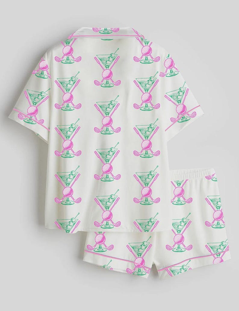 May include: White pajama set with a repeating pattern of pink golf clubs, golf balls, and green martini glasses. The set includes a short-sleeved button-up shirt and matching shorts, both trimmed with pink piping.