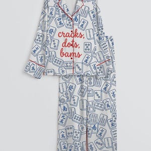 May include: White pajama set with a blue Mahjong tile pattern and red trim. The top features the text "cracks, dots, bams" in red. The set includes a button-down shirt and matching pants.