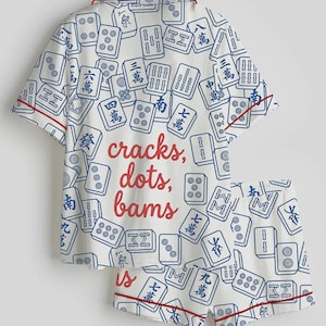 May include: White pajama set with a pattern of blue Mahjong tiles. The set includes a short-sleeved top and shorts, both trimmed with red piping. The text "cracks, dots, bams" is printed on the top.