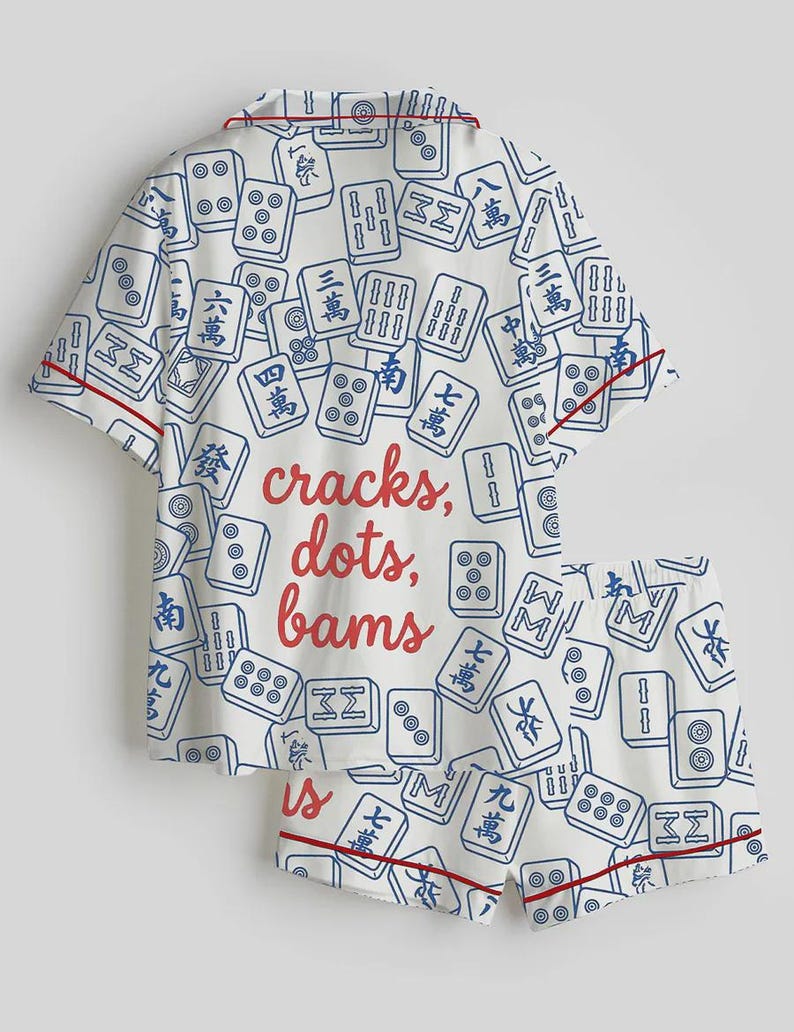 May include: White pajama set with a pattern of blue Mahjong tiles. The set includes a short-sleeved top and shorts, both trimmed with red piping. The text "cracks, dots, bams" is printed on the top.