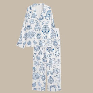 Puede incluir: Conjunto de pijama blanco con un patrón de garabatos azules con temática de boda. La parte superior de manga larga tiene cuello y cierre de botones. Los pantalones son largos. El patrón incluye pasteles, anillos y coches de boda.