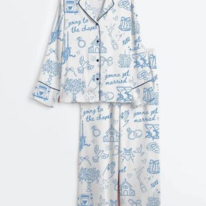 Può includere: Un set di pigiama bianco con una stampa a linee blu che raffigura icone a tema nuziale come cappelle, anelli, auto e calici di champagne. Il tessuto è decorato con il testo "going to the chapel" e "gonna get married" in un carattere corsivo.