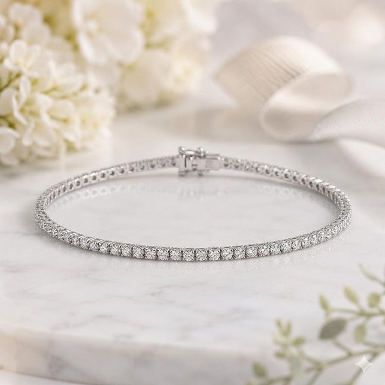 May include: A silver-toned tennis bracelet featuring a continuous row of small, round, clear stones set in a metallic frame. The bracelet includes a secure box clasp mechanism at the top, showcasing a uniform design throughout the entire piece.