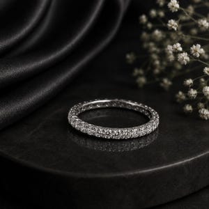 Op de afbeelding: Een zilverkleurige eternity ring met een doorlopende rij kleine, ronde, heldere gefacetteerde stenen die langs de gehele omtrek van de metalen band zijn gezet, wat zorgt voor een uniforme en sprankelende uitstraling van het sieraad.
