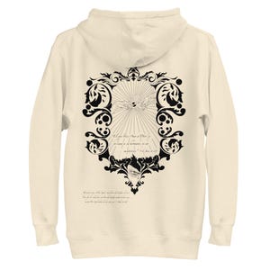 May include: Cream-coloured zip-up hoodie with a black ornate design on the back. The design features two hands reaching out, within a decorative frame and text. The hoodie has a hood and a full zip.