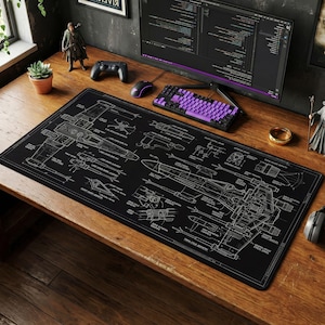 May include: A black rectangular desk mat featuring a detailed blueprint design of a starfighter. The blueprint is rendered in white lines against a black background. The mat is on a wooden desk with a computer, keyboard, and other accessories.