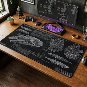 May include: Black rectangular desk mat featuring detailed white schematics of a spaceship. The mat includes text and is surrounded by a computer, keyboard, mouse, and other desk accessories. The desk is made of wood.