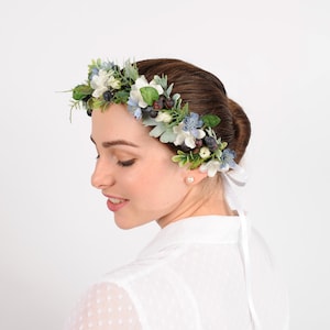 A bride wears a circlet headband tied with ribbons at the back. Soft blue woodland flowers are placed with dark blue berries, greyish leaves, ferns and a scattering of other white florals to make this flower crown. Adjustable and fits most age groups