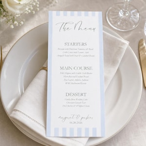 Pode incluir: Um cartão de menu de casamento alto e retangular com listras verticais azul-claras nas laterais. O texto diz The Menu, Starters, Main Course, Dessert, e os nomes Margaret & Parker com a data 20/06/2026 em fonte manuscrita e serifada.