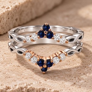 May include: A two-piece ring set featuring a chevron-shaped design. The bands are crafted from silver and rose gold tones, accented with round-cut deep blue sapphires and clear white diamonds arranged in a symmetrical, pointed cluster pattern.