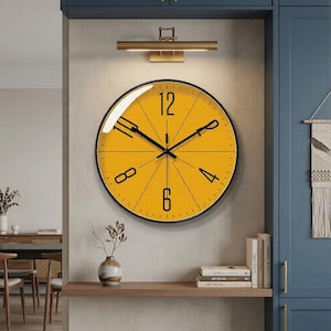 Puede incluir: Un reloj de pared grande y redondo con una esfera amarilla brillante y manecillas y números negros. El reloj tiene un marco de metal negro y está montado en una pared de color claro. El reloj es un elemento decorativo en una habitación.