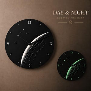 May include: Two black wall clocks with a celestial design. One clock shows a white and black planet design with stars, while the other glows green in the dark. The clocks have the numbers 3, 6, 9, and 12.