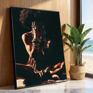 May include: A framed art print featuring a person with an afro, seated with hands covering their face. The person is adorned with gold bracelets and rings. The print is in a black frame, leaning against a wooden wall, with a plant and ocean view in the background.