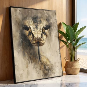 Könnte beinhalten: Gerahmtes Kunstwerk mit einer Nahaufnahme des Kopfes einer Schlange. Die Schlange hat ein braunes und schwarzes Muster mit gelben Augen und einer gegabelten schwarzen Zunge. Das Kunstwerk befindet sich in einem schwarzen Rahmen und wird in der Nähe eines Fensters mit einer Pflanze ausgestellt.