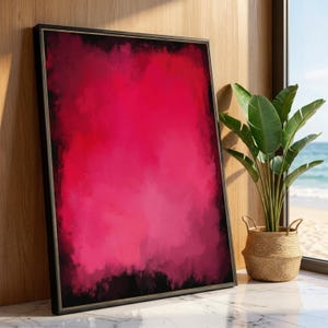 Puede incluir: Impresión artística enmarcada con un degradado de tonos rosas y rojos y un borde oscuro. La obra de arte está en un marco negro, apoyada contra una pared de madera. Una planta en maceta está cerca.