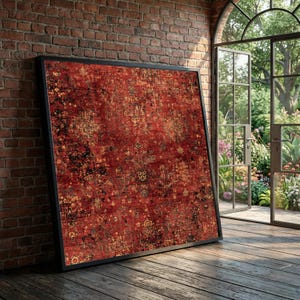 May include: A large, framed rug with a traditional design. The rug features a deep red background with intricate patterns in gold, black, and cream. The frame is black, and the rug is leaning against a brick wall. The scene is illuminated by natural light.