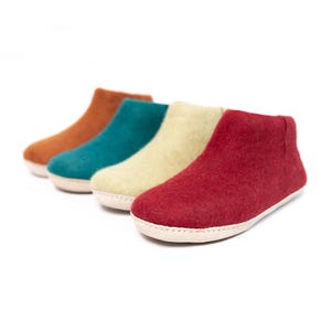 May include: Four pairs of felt slippers in different colors: brown, teal, beige, and red. The slippers have a white rubber sole.