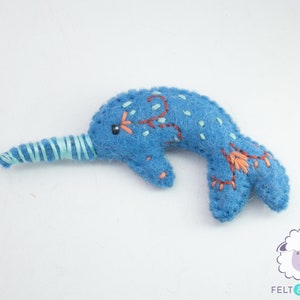 May include: A blue felt narwhal with a light blue felt horn and embroidered details. The narwhal is a popular sea creature and a whimsical addition to any child's room.