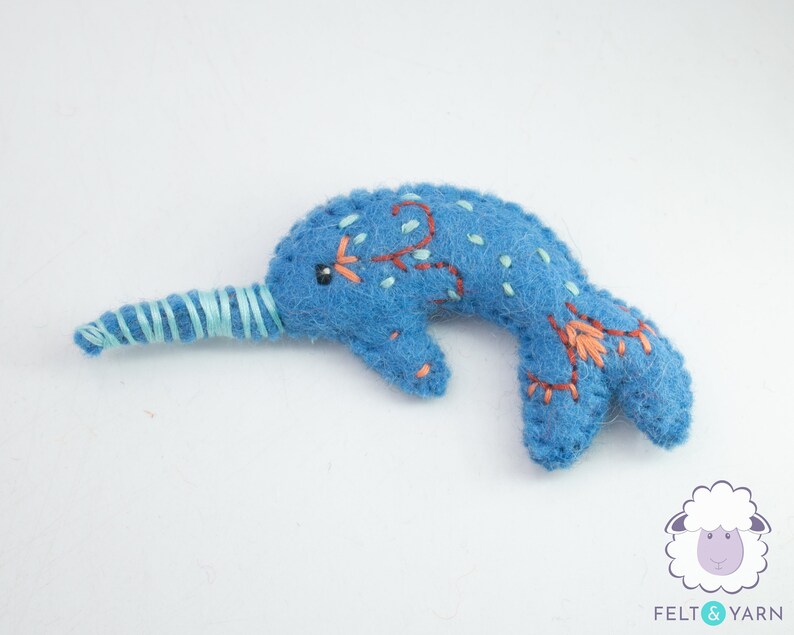 May include: A blue felt narwhal with a light blue felt horn and embroidered details. The narwhal is a popular sea creature and a whimsical addition to any child's room.